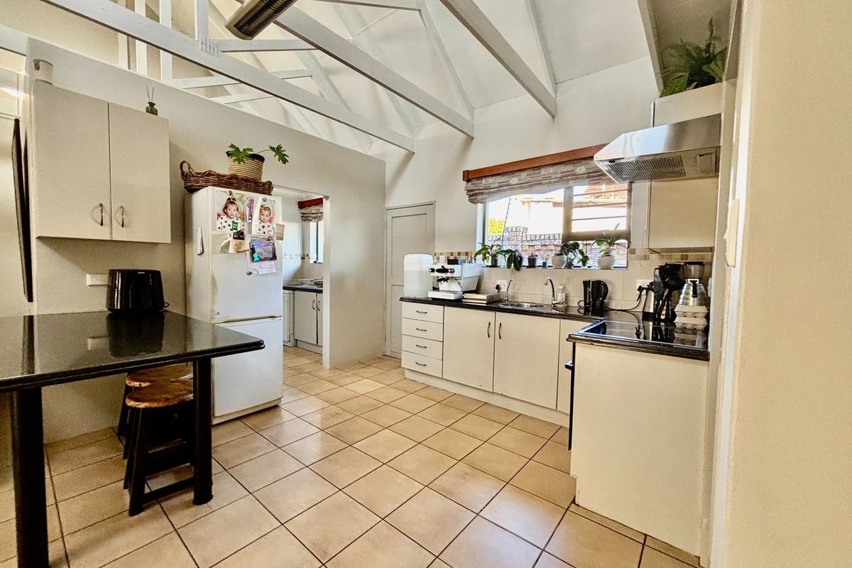 A functional kitchen featuring exposed timber rafters, granite countertops, built-in cabinetry, and tiled flooring, with an adjacent scullery area visible.