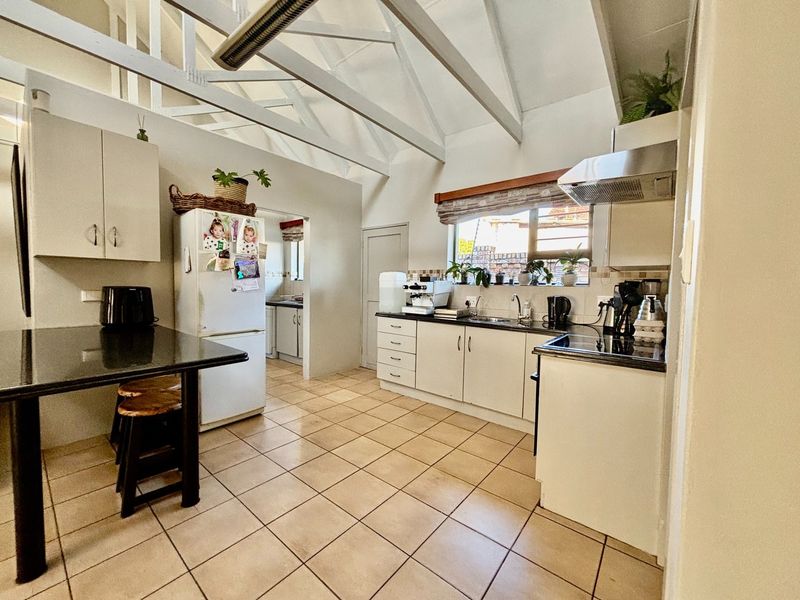 A functional kitchen featuring exposed timber rafters, granite countertops, built-in cabinetry, and tiled flooring, with an adjacent scullery area visible.