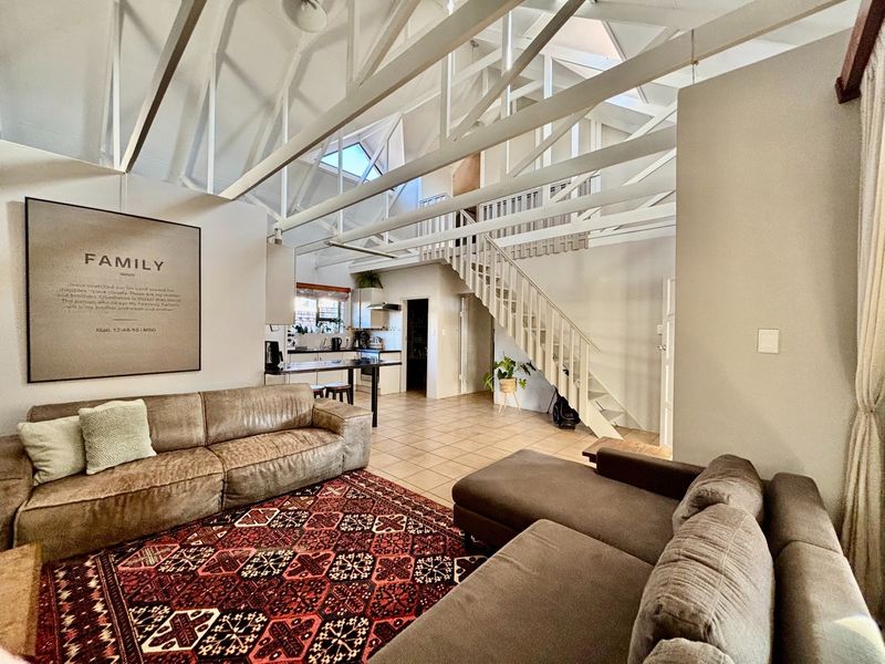 Spacious open-plan living area featuring high vaulted ceilings with exposed trusses, a mezzanine level, tiled floors, and an integrated kitchen.