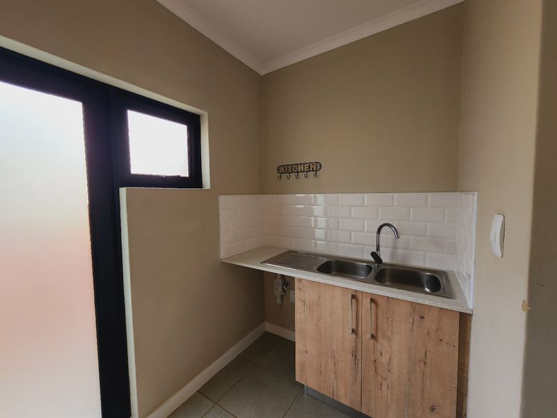 A compact scullery area featuring a double bowl stainless steel sink, modern subway tile backsplash, and wood-look cabinetry with stone countertops.