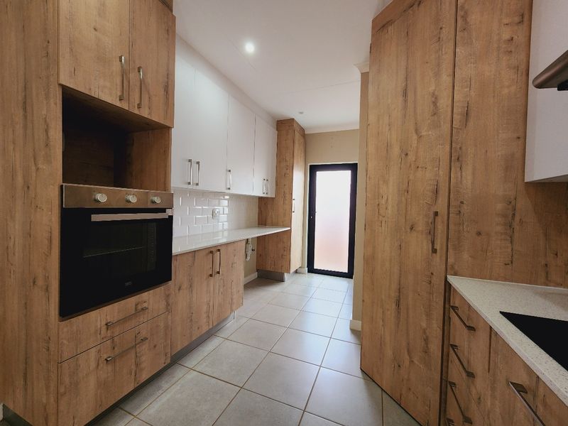 Modern kitchen featuring wood-look cabinetry, white subway tile backsplash, quartz countertops, and a built-in oven, leading to an exterior door.