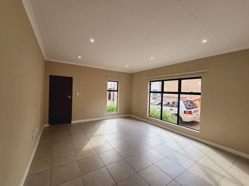 A bright, empty living area featuring neutral tiled flooring, modern recessed downlights, and large aluminium-framed windows providing natural light.