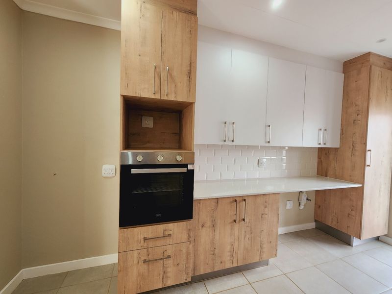Modern kitchen featuring wood-look laminate cabinetry, white subway tile backsplash, stone countertops, and a built-in oven.