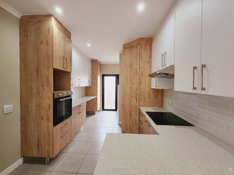 Modern kitchen featuring wood-look and white cabinetry, stone countertops, built-in oven, electric hob, and subway tile backsplash with neutral tiled flooring.