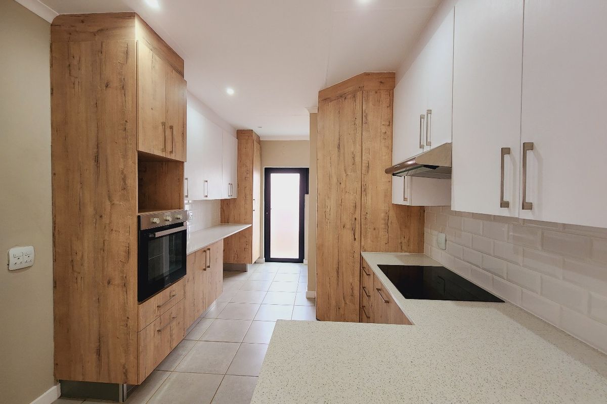 Modern kitchen featuring wood-look and white cabinetry, stone countertops, built-in oven, electric hob, and subway tile backsplash with neutral tiled flooring.