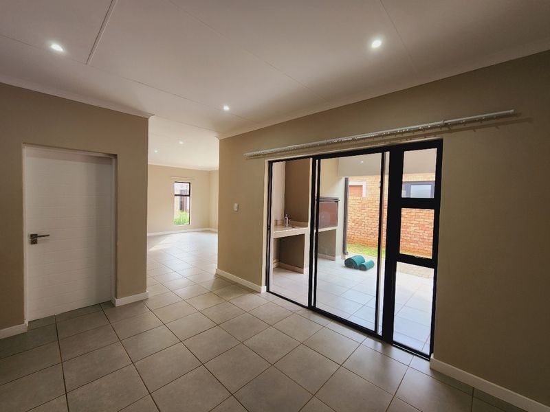 Spacious open-plan living area featuring neutral tiled floors, recessed lighting, and large sliding doors providing seamless access to a covered patio with built-in braai.