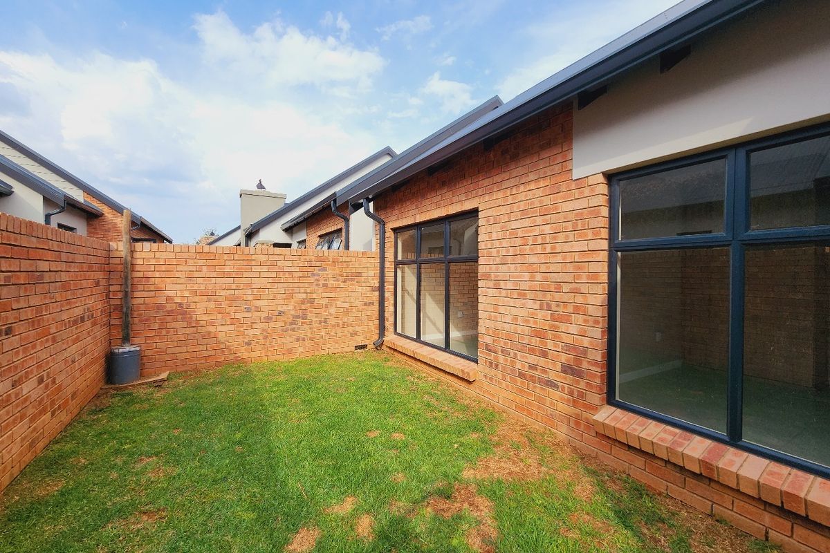 A private rear garden area featuring face brick exterior walls, dark aluminium window frames, and a small lawn enclosed by a boundary wall.