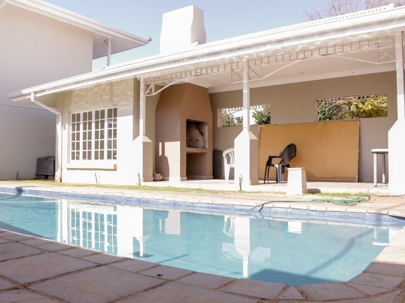 Outdoor pool area featuring a covered patio with a built-in braai, ideal for entertaining and relaxation.