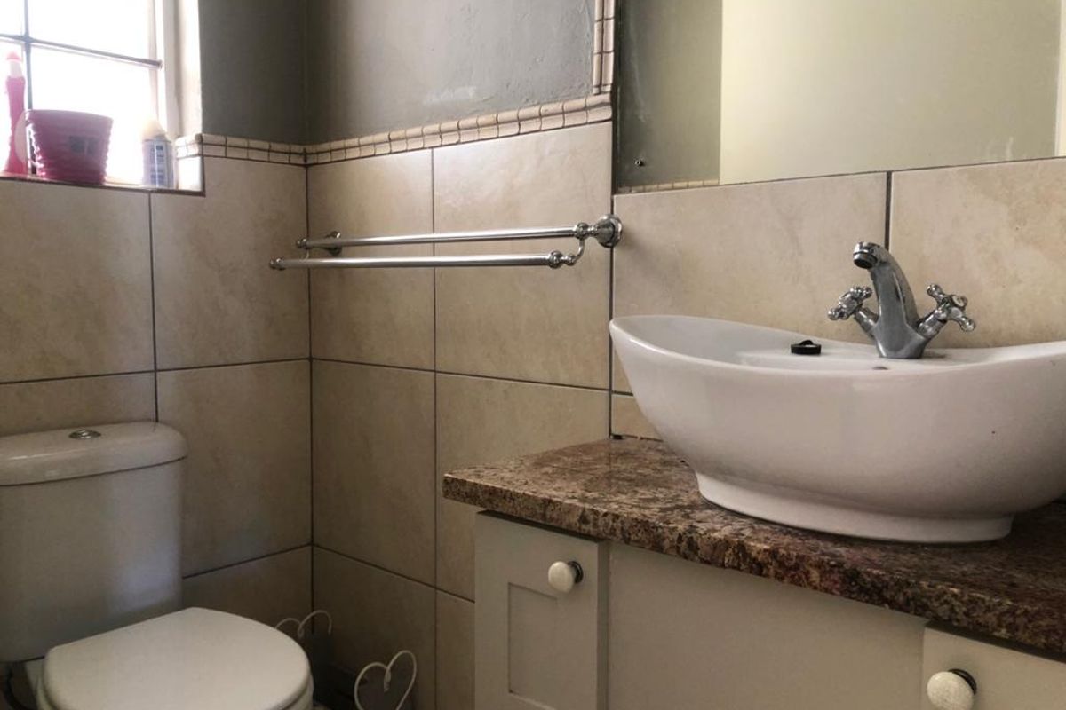 A functional bathroom featuring a vessel sink on a granite vanity countertop, ceramic wall tiling, and a standard close-coupled toilet.