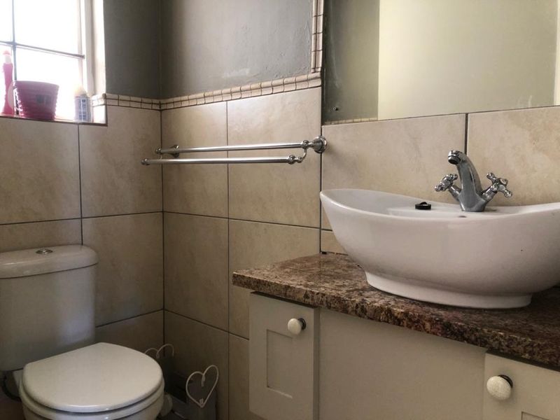 A functional bathroom featuring a vessel sink on a granite vanity countertop, ceramic wall tiling, and a standard close-coupled toilet.