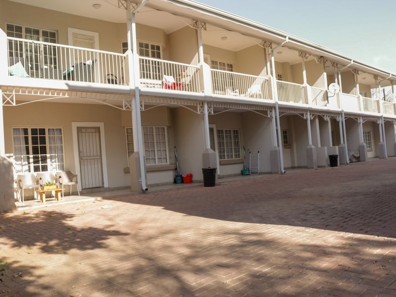Exterior view of a multi-story apartment complex featuring a paved driveway, ground-level patio access, and upper-level balconies with metal railings.