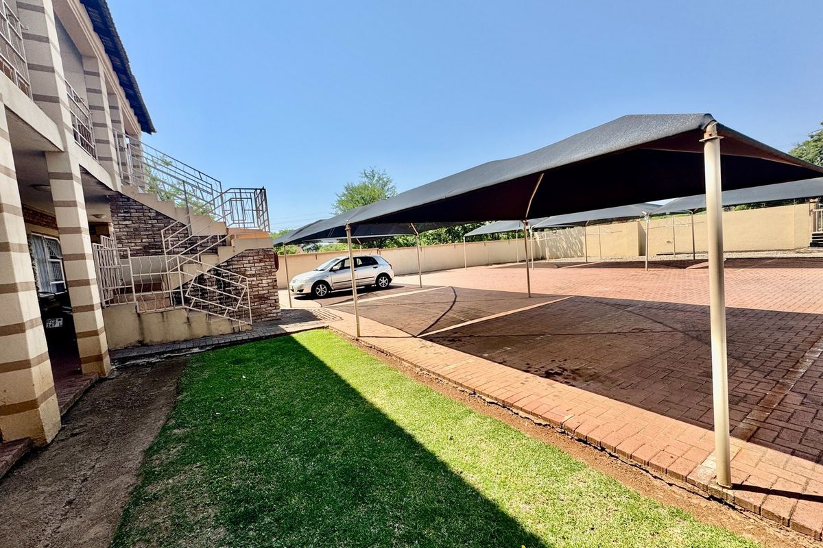 Rear exterior view of the apartment complex featuring a paved parking area with shade cloth carports and an external staircase.