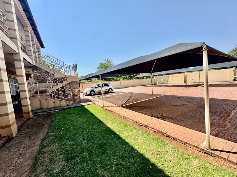 Rear exterior view of the apartment complex featuring a paved parking area with shade cloth carports and an external staircase.