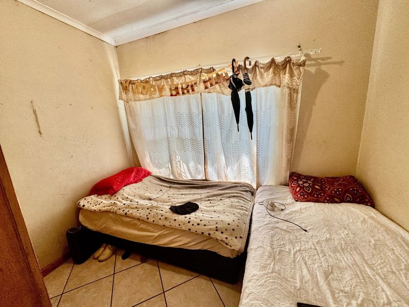 A compact bedroom featuring tiled flooring and a window with a curtain rod, currently showing signs of wear on the wall surfaces.