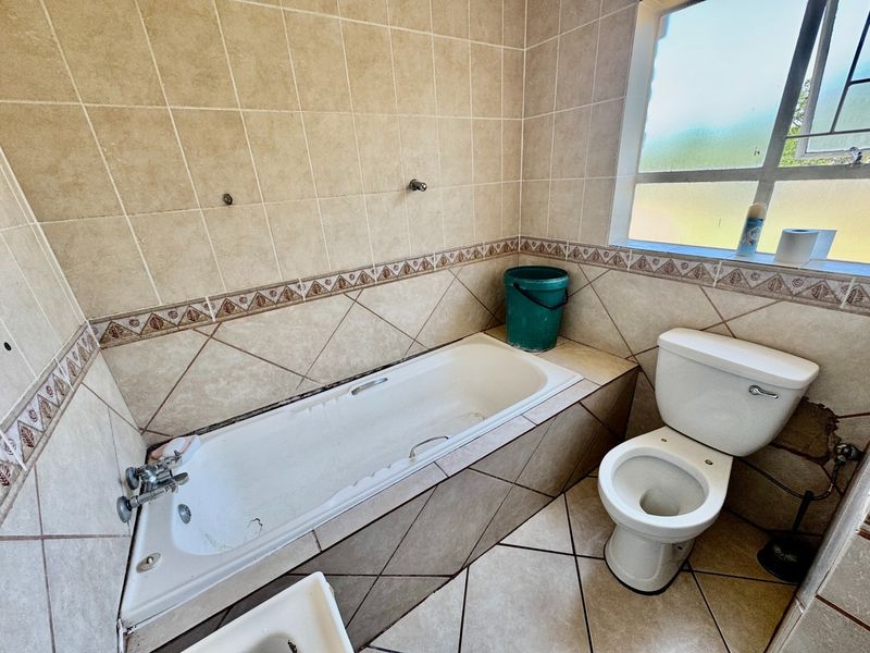A dated bathroom featuring a built-in bathtub, standard toilet, and neutral ceramic tiling throughout, requiring cosmetic updates to improve its overall condition.