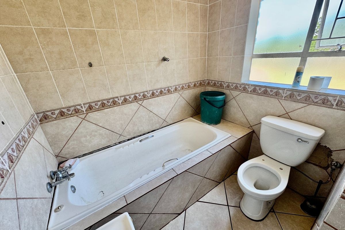A dated bathroom featuring a built-in bathtub, standard toilet, and neutral ceramic tiling throughout, requiring cosmetic updates to improve its overall condition.