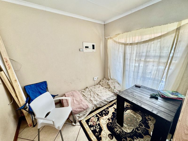 A compact bedroom featuring tiled flooring and a wall-mounted electrical distribution board, requiring cosmetic updates to improve its overall condition.