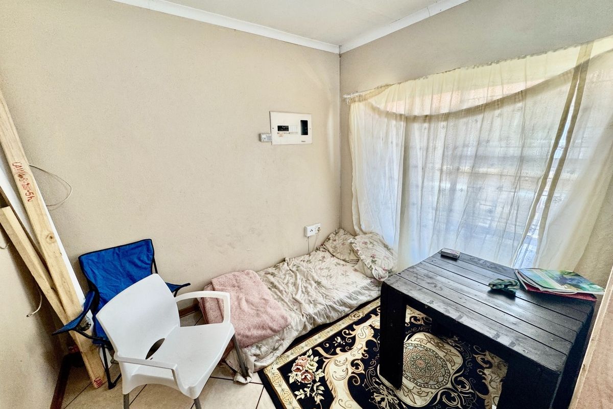 A compact bedroom featuring tiled flooring and a wall-mounted electrical distribution board, requiring cosmetic updates to improve its overall condition.