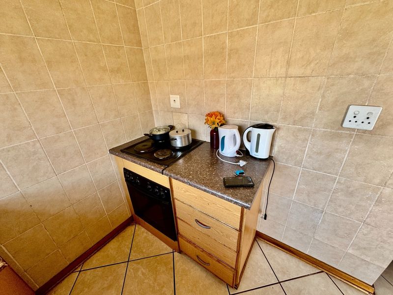 Compact kitchen corner featuring a built-in oven, electric hob, wooden cabinetry, and neutral ceramic wall and floor tiling.