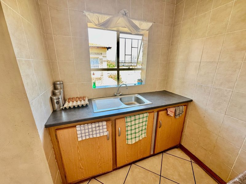 A functional scullery area featuring a stainless steel sink, laminate countertop, wooden cabinetry, and tiled finishes throughout.