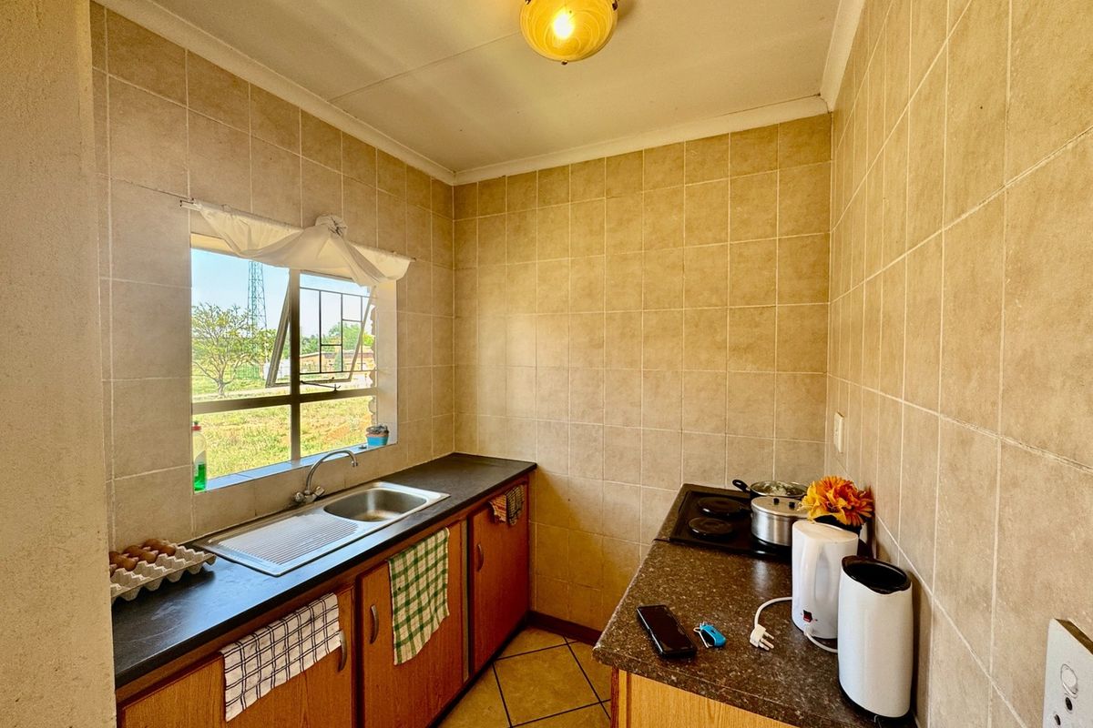 Compact kitchen featuring tiled walls, laminate countertops, built-in cabinetry, and an electric hob, offering a functional layout with natural light.
