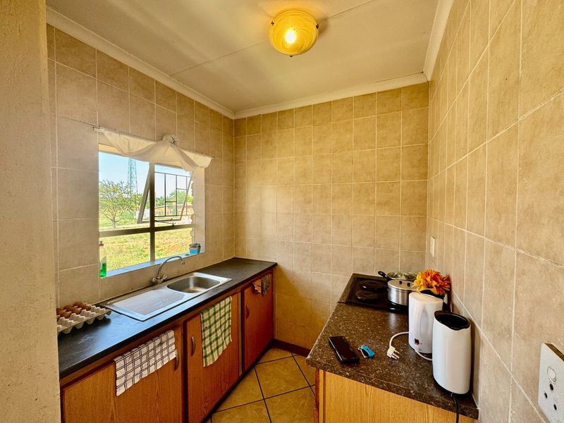 Compact kitchen featuring tiled walls, laminate countertops, built-in cabinetry, and an electric hob, offering a functional layout with natural light.
