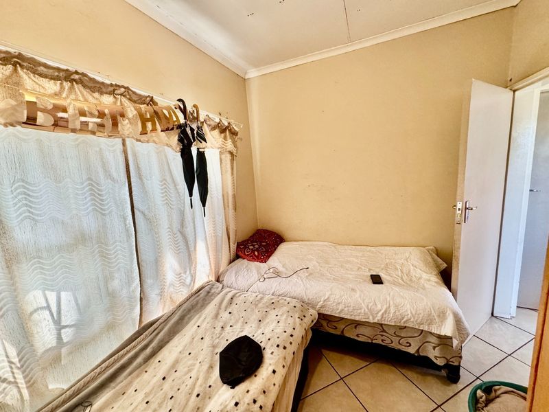 A compact bedroom featuring tiled flooring and coved ceiling details, requiring cosmetic updates to the wall and ceiling finishes.