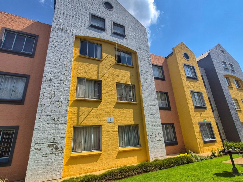 Exterior view of a multi-story apartment complex featuring colorful painted brick facades, casement windows with security bars, and a well-maintained lawn area.