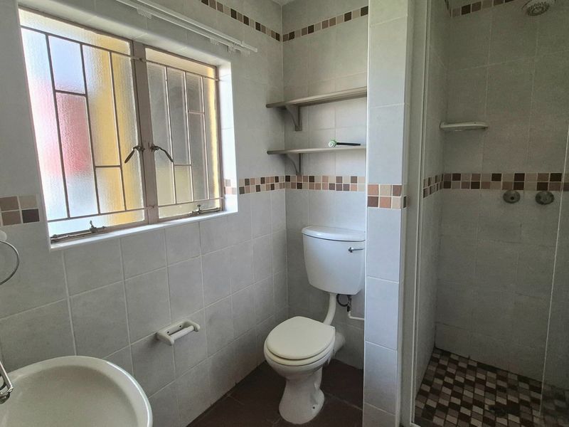 A functional bathroom featuring a shower enclosure, toilet, and washbasin with neutral wall tiling and built-in shelving.