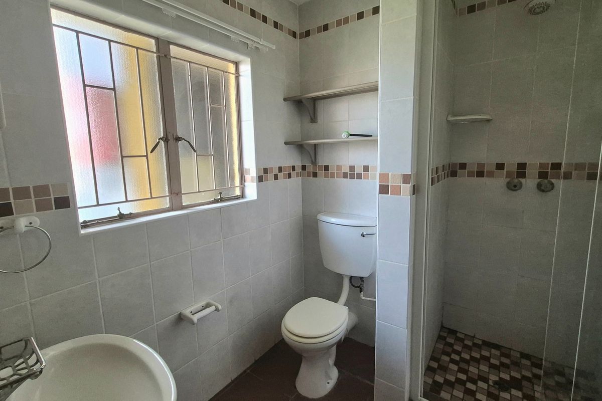 A functional bathroom featuring a shower enclosure, toilet, and washbasin with neutral wall tiling and built-in shelving.