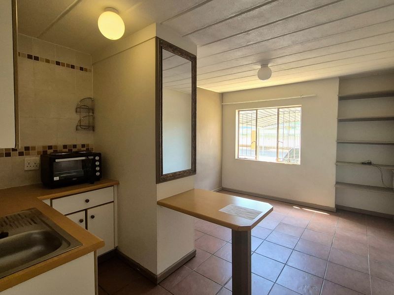 Open plan kitchen and living area featuring tiled flooring, built-in shelving, and a breakfast counter, offering a functional and versatile living space.