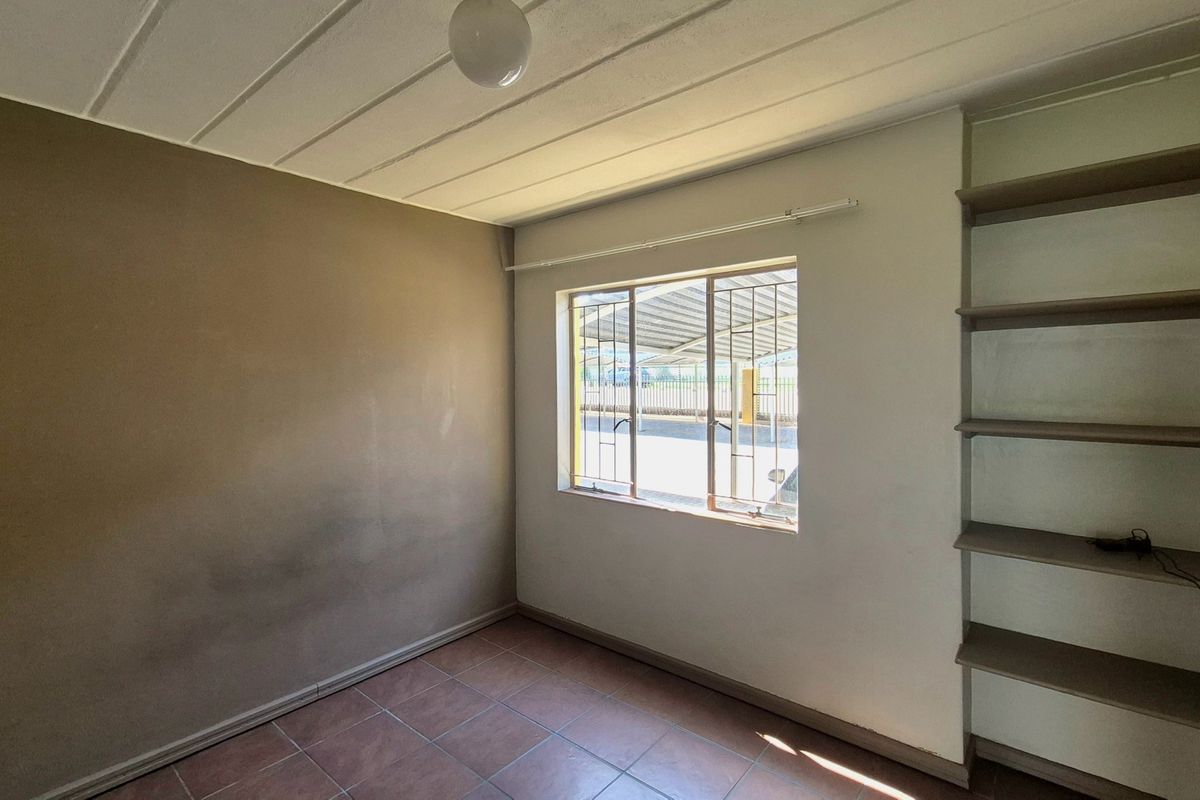 An empty bedroom featuring tiled flooring, built-in shelving, and security bars on the window, requiring cosmetic updates to the wall finishes.