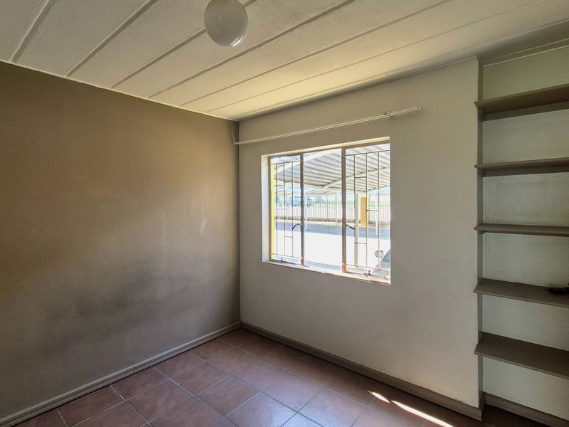 An empty bedroom featuring tiled flooring, built-in shelving, and security bars on the window, requiring cosmetic updates to the wall finishes.