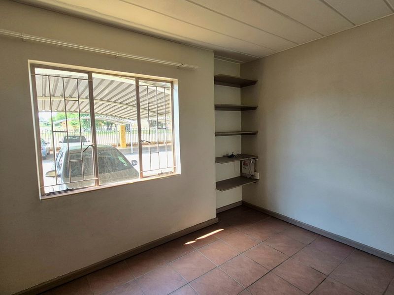 An empty bedroom featuring tiled flooring, built-in wall shelving, and a window with security bars overlooking the parking area.
