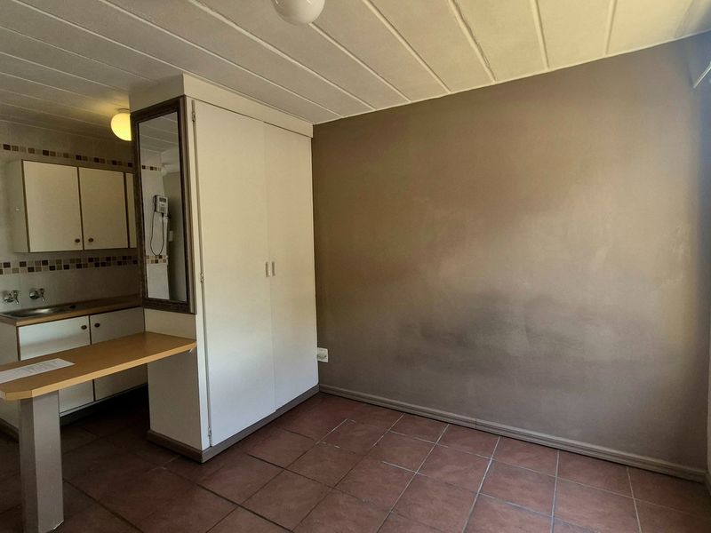 An open-plan living and kitchen area featuring tiled flooring, built-in cabinetry, a breakfast counter, and a built-in cupboard, requiring cosmetic updates.