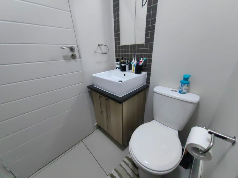 A compact bathroom featuring a modern vessel sink on a vanity cabinet, a toilet, and tiled splashback detailing.