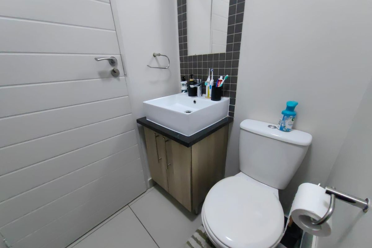 A compact bathroom featuring a modern vessel sink on a vanity cabinet, a toilet, and tiled splashback detailing.