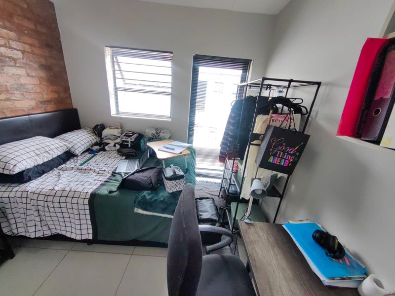 A bedroom featuring an exposed brick accent wall, tiled flooring, and natural light through aluminium-framed windows and a door.