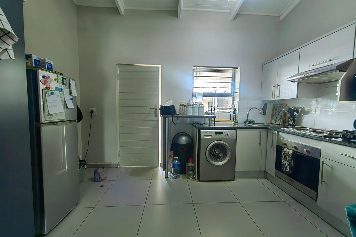 A functional kitchen featuring built-in cabinetry, stainless steel appliances, tiled flooring, and an exposed beam ceiling with direct access to an exterior door.