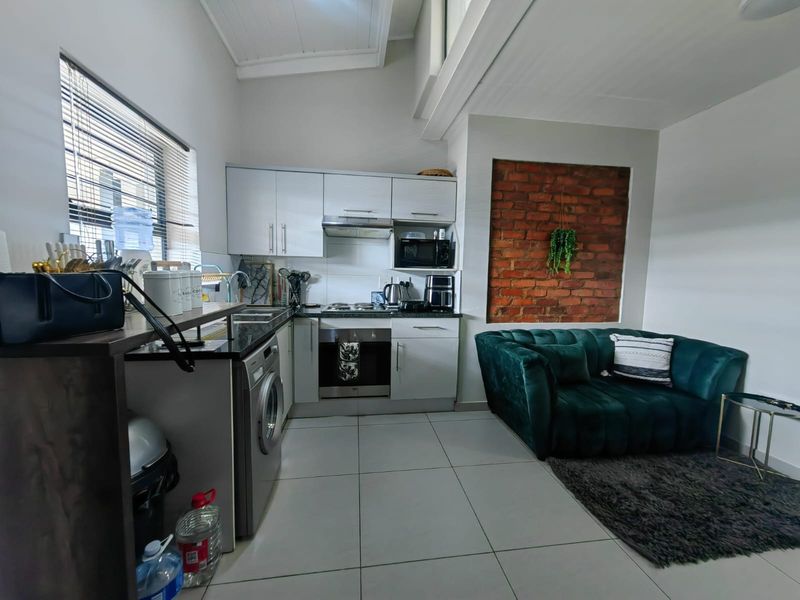 Open-plan living area featuring a modern kitchen with built-in appliances, tiled flooring, and a striking exposed brick feature wall under a vaulted ceiling.