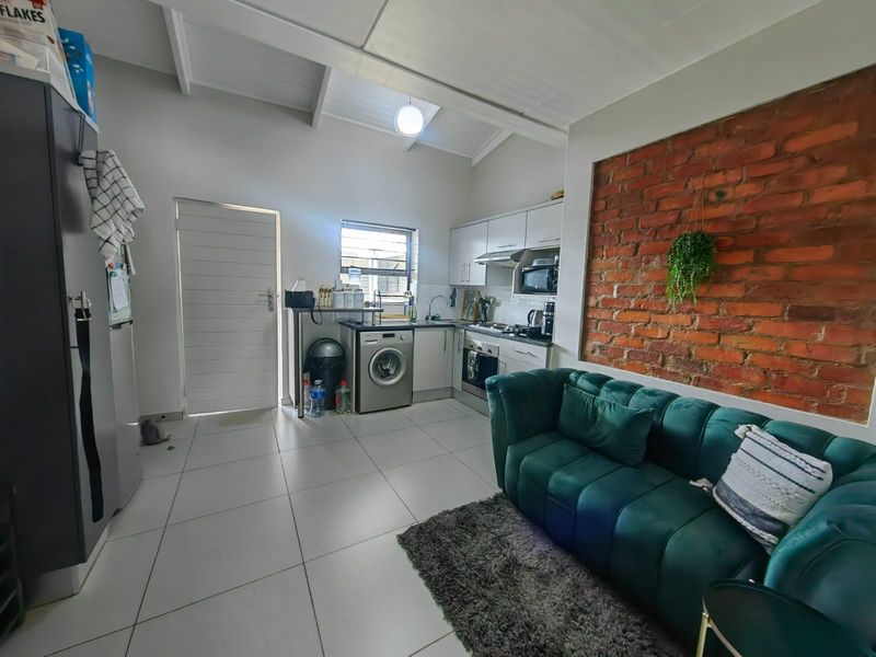 Open-plan living area featuring a striking exposed brick wall, tiled flooring, and a compact kitchen with built-in cabinetry and appliances.