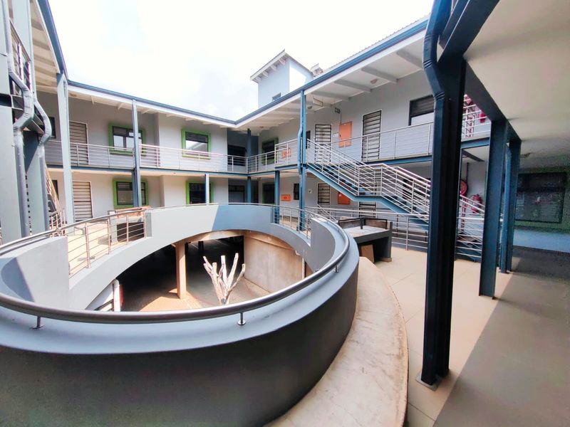 A multi-level apartment complex courtyard featuring a central circular design, steel staircases, and open-air walkways with modern stainless steel balustrades.