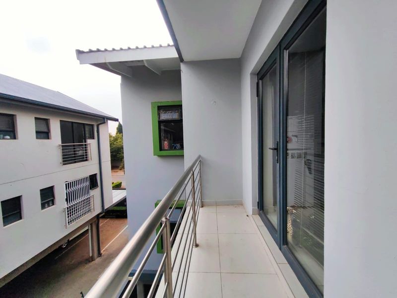 A clean, modern balcony featuring tiled flooring and a stainless steel balustrade, providing an outdoor extension to the apartment living space.