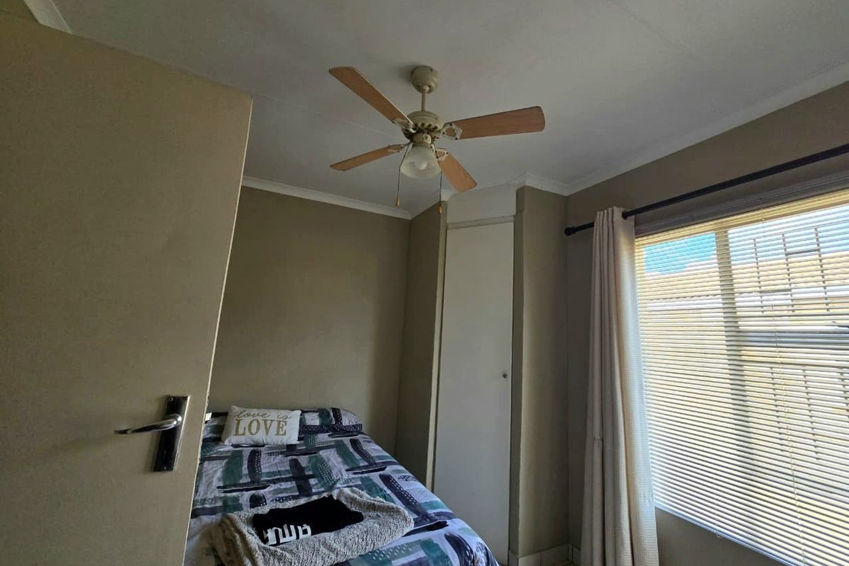 A functional bedroom featuring a ceiling fan, built-in storage cupboard, and tiled flooring, offering a neutral base for personalization.