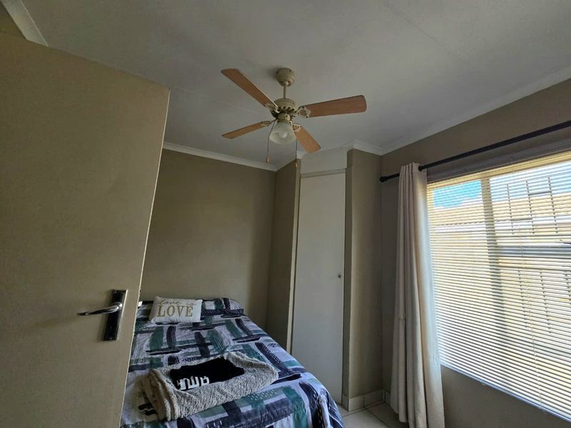 A functional bedroom featuring a ceiling fan, built-in storage cupboard, and tiled flooring, offering a neutral base for personalization.