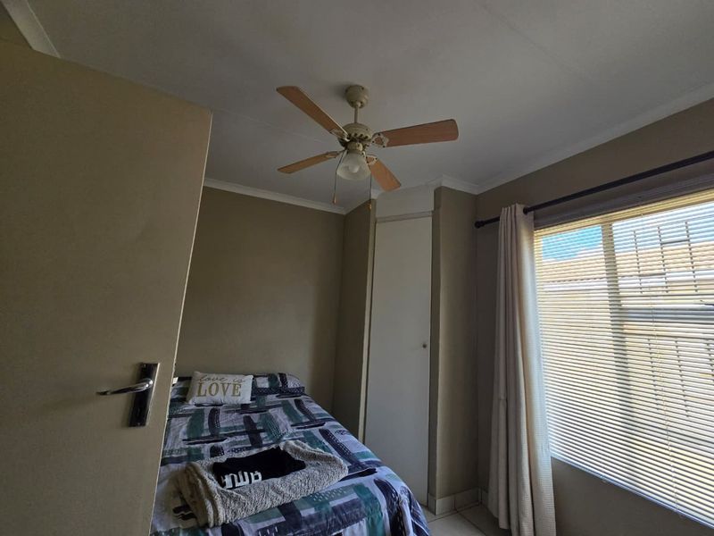 A functional bedroom featuring a ceiling fan, built-in cupboard storage, and window blinds, providing a comfortable and practical living space.