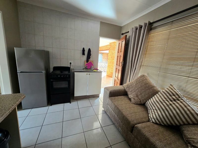 Compact open-plan living area featuring a kitchenette with tiled flooring, built-in cabinetry, a sink, and a freestanding stove, with direct access to an outdoor space.