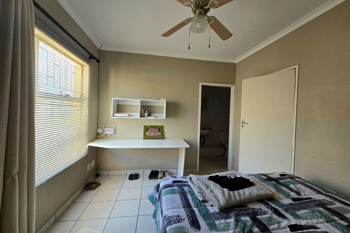 A functional bedroom featuring tiled flooring, a ceiling fan, built-in desk space, and direct access to an en-suite bathroom.