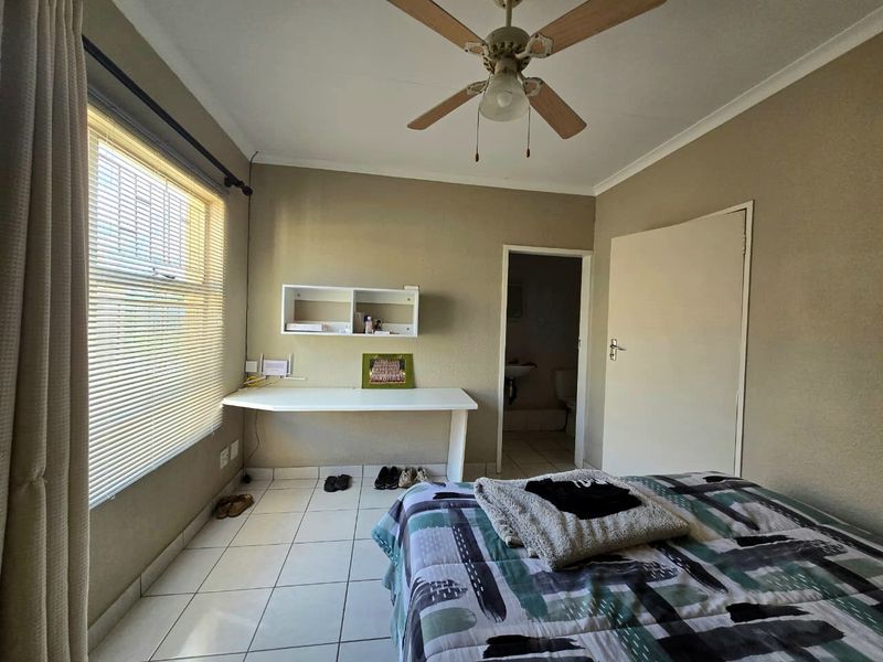 A functional bedroom featuring tiled flooring, a ceiling fan, built-in desk space, and direct access to an en-suite bathroom.