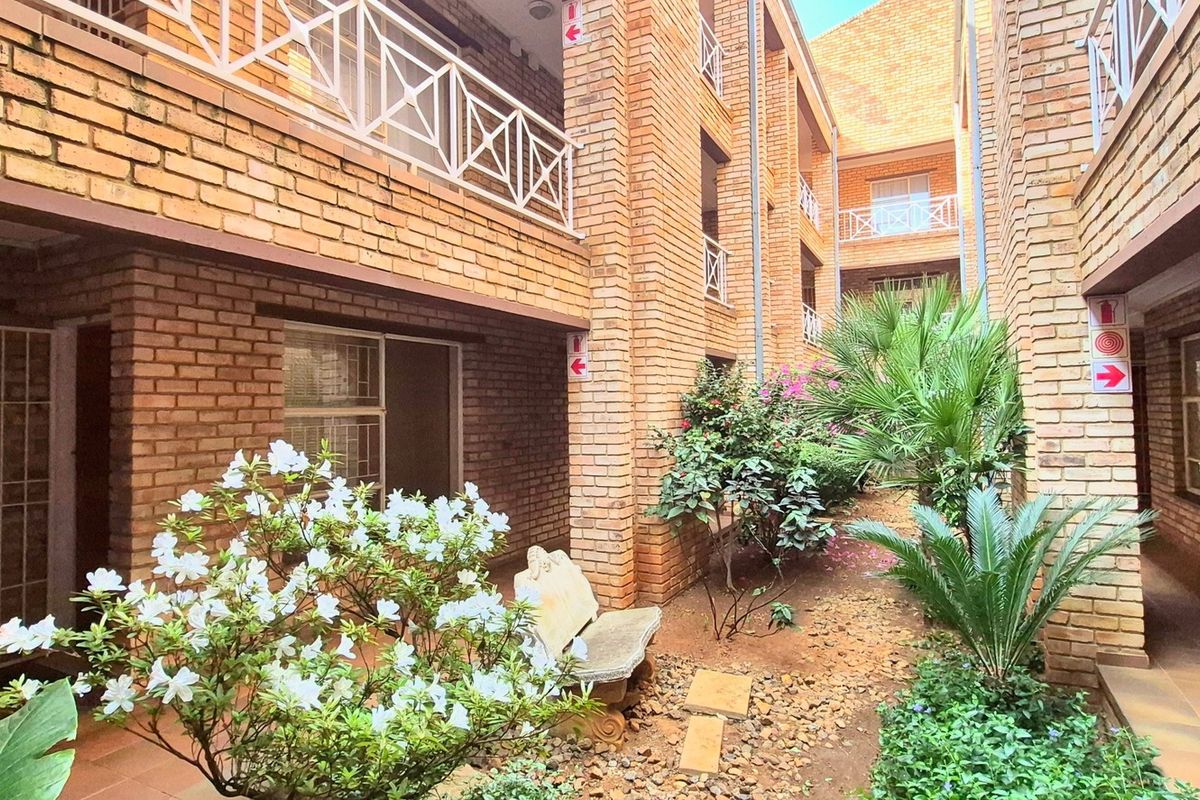 A view of the apartment complex courtyard featuring face brick architecture, tiled walkways, and established garden beds.